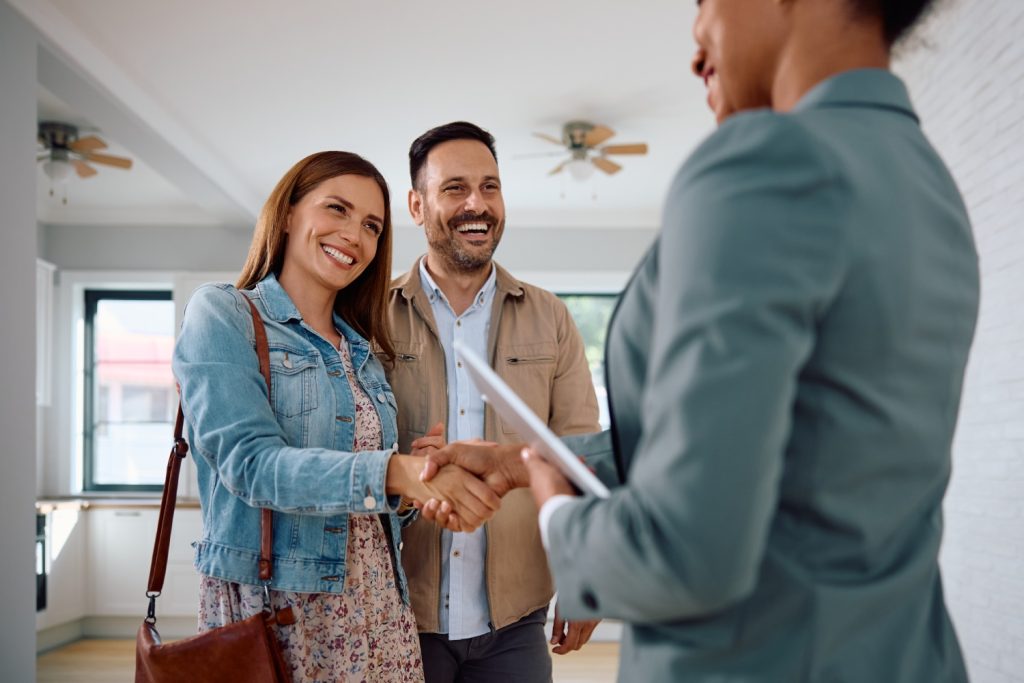 Happy woman shaking hands with real estate agent while buy new home with her husband.