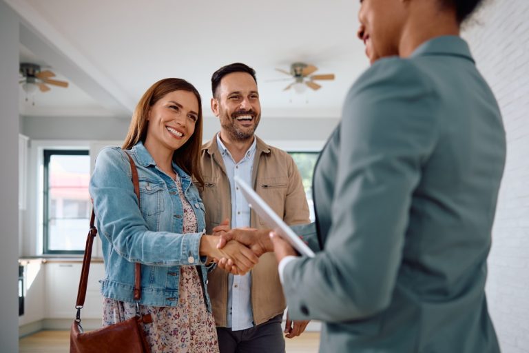 Happy woman shaking hands with real estate agent while buy new home with her husband.